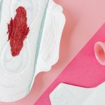 Close-up of menstrual products including pad and cup on a pink surface for period care.