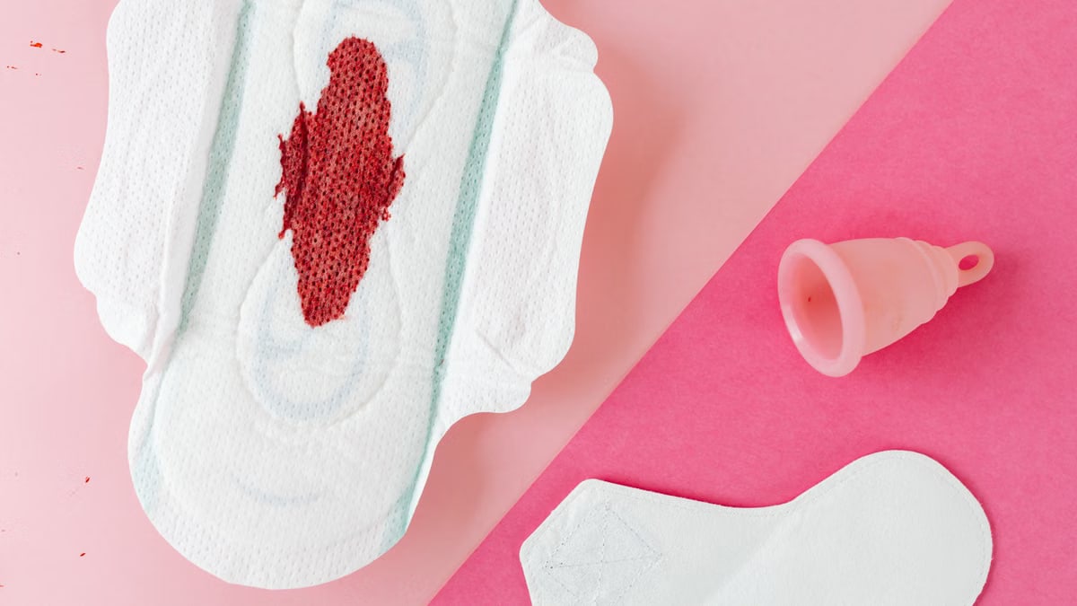 Close-up of menstrual products including pad and cup on a pink surface for period care.
